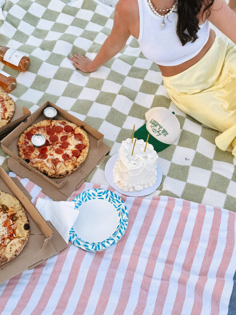 Eine Frau sitzt auf einer Picknickdecke mit Pizza und Kuchen.