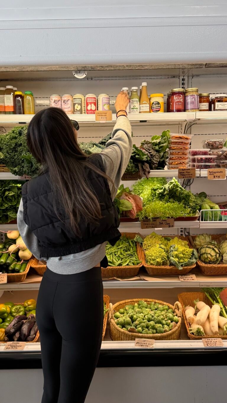 Eine schlanke Frau steht vor einem Supermarktregal voller Gemüse.